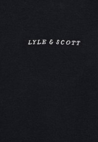 Tissu en coton noir avec une surface texturée présentant le texte "LYLE & SCOTT" brodé en blanc, centré sur le matériau.