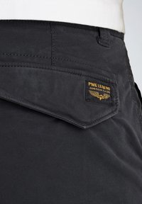 Pantalones de algodón negros con un bolsillo delantero que presenta una etiqueta de PME Legend. La tela es suave con un ligero brillo, mostrando costuras precisas.
