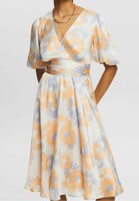 Robe portefeuille fleurie blanche, ornée de motifs floraux abstraits en orange et bleu clair, avec des manches courtes et une taille cintrée.