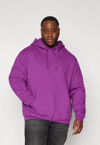 Purple hooded sweatshirt with a front pouch pocket, drawstring hood, and ribbed cuffs. Worn with dark gray jeans.