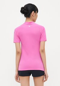 Pink short-sleeve athletic top with a high neckline. Made of smooth, stretchy material. Features a small logo on the upper back.
