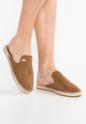 Chaussures espadrilles en daim marron à enfiler avec semelles en jute tressée portées pieds nus sur fond blanc.