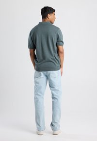 Polo verde de manga corta con cuello clásico, combinado con jeans de mezclilla azul claro. La tela parece suave y tiene un corte relajado.