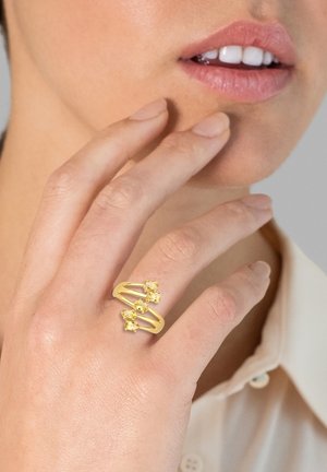 Guldring med en snoet bænk, der har tre gule ædelstene. Designet er åbent og moderne, med en glat, blank finish.