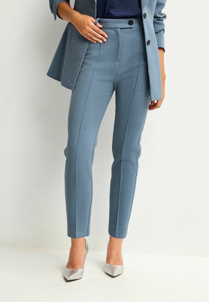 Helleblaue maßgeschneiderte Hose mit glatter Textur, hoch tailliert, mit Seitennähten und schmaler Passform. Kombiniert mit silbernen spitzen Absätzen.