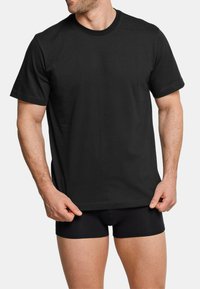 T-shirt nera in cotone con maniche corte, colletto rotondo e orlo dritto. Indossata con boxer neri, caratterizzati da una trama liscia e un design minimal.