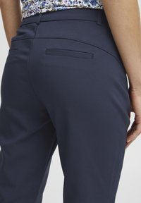 Marineblauwe broek met een gladde textuur, slim fit en twee achterzakken, met subtiele naden voor extra detail.