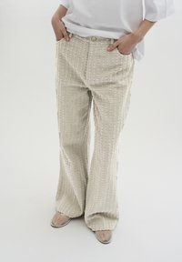 Beige Schlaghose mit strukturierten vertikalen Streifen, mit Knopfverschluss und Taschen. Der Stoff hat ein leicht erhabenes Muster.