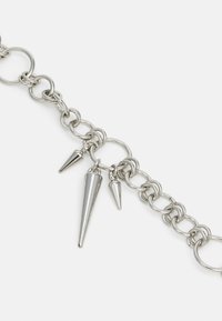 Bracciale in argento con anelli circolari misti. Presenta tre charm metallici appuntiti di diverse dimensioni, che aggiungono texture e dettaglio.
