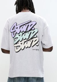 Light gray oversized t-shirt featuring a bold, multicolored graphic with stylized text on the back. Short sleeves and soft texture.