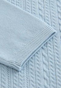 Svetlo modro pleteno blago z vzorcem kavljastega pletenja, prikaz bližnjice manšete z rebrasto teksturo.