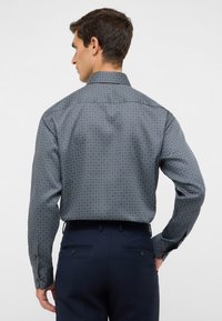 Blau gemustertes Hemd mit umlegtem Kragen, das ein geometrisches Design aufweist. Lange Ärmel mit Knopfmanschetten, getragen mit einer navyblauen Hose.