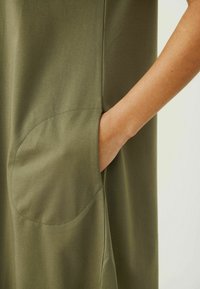 Vestido verde oliva con una textura suave, que presenta un bolsillo curvado en el costado y detalles de costura limpia.
