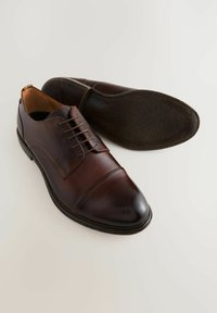 Chaussures habillées en cuir marron avec un bout arrondi, six œillets pour les lacets et une semelle texturée. Présente des accents de couture discrets.