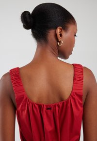 Rode mouwloze kleding met een gestructureerde, geraffineerde achterkant en een brede halslijn. Heeft een klein label nabij de halslijn en een gladde stof.