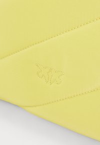 Κίτρινο ύφασμα με υφή ενοποιημένου σχεδίου που διαθέτει κεντημένο λογότυπο. Οι ραμμένες λεπτομέρειες ενισχύουν τα σχεδιαστικά χαρακτηριστικά της δομής.