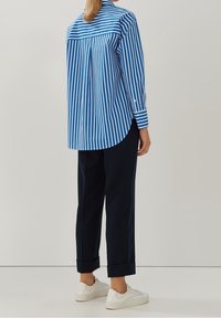 Modrá a bílá pruhovaná košile s knoflíky a zakřiveným lemem, zkombinovaná s námořnickými kalhotami a bílými teniskami. Košile má dlouhé rukávy.