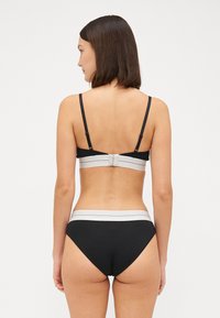 Zwarte bh en bijpassende slip met een brede grijze elastische band. De achterkant heeft verstelbare banden en een haaksluiting op de bh.