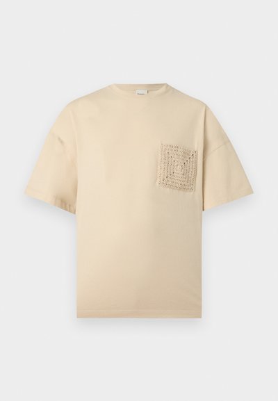 Μπεζ κοντομάνικο μπλουζάκι με στρογγυλή λαιμόκοψη και υφασμένη πλεκτή τετράγωνη τσέπη στο αριστερό στήθος.