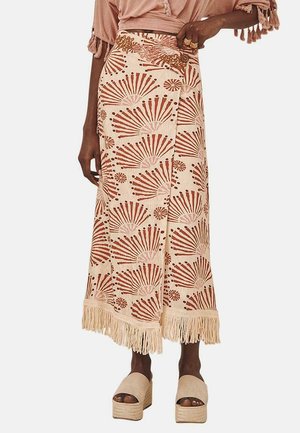 Falda maxi hecha de tela liviana, con una base crema y patrones de abanico terracota, y un dobladillo con flecos. Complementada con zapatos de plataforma.