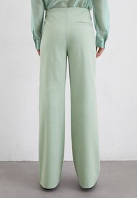 Brede broek in zacht mintgroen stof. Kenmerkt zich door een gladde textuur, hoge taille en een enkele achterzak. Eenvoudig en modern ontwerp.