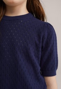 Tumesinine salle kudumispullover, millel on tekstuuriline muster, lühikesed puffvarrukad ja ribaga kaelus. Kude on kerge ja hingav.