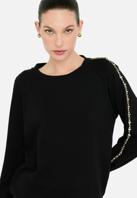Zwarte sweatshirt met een ronde halslijn en een relaxte fit, voorzien van gouden accenten langs de schoudernaad voor extra detail.