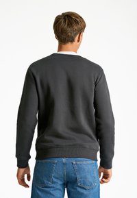 Sudadera negra de cuello redondo con puños y dobladillo acanalados, hecha de un tejido suave y texturizado, combinada con jeans de denim azul claro.