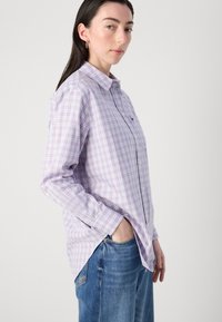 Light purple and pink checkered button-up shirt, long sleeves, cotton material, paired with blue jeans, featuring a small logo on the chest.