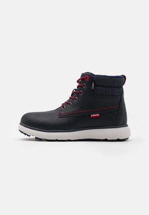 Bottine en cuir noir avec semelle blanche, lacets rouges, couture rouge, col en denim et petite étiquette rouge Levi's sur le côté.