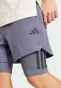 Ljubičaste sportske kratke hlače s crnim naglascima, koje imaju unutarnju podlogu i tri vertikalne pruge sa strane. Materijal s teksturiranim dizajnom.