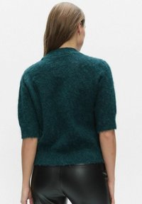 Lyijynsininen lyhythihainen neulepusero, pörröinen pinta, pyöreä pääntie, hieman lyhennetty malli, raakareunalla, yhdistetty mustien nahkahousujen kanssa.