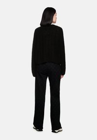 Schwarzer strukturierten Strickpullover mit einem verkürzten Design, kombiniert mit schwarzen Hosen mit einem dezenten Sternmuster und schwarzen Schuhen.