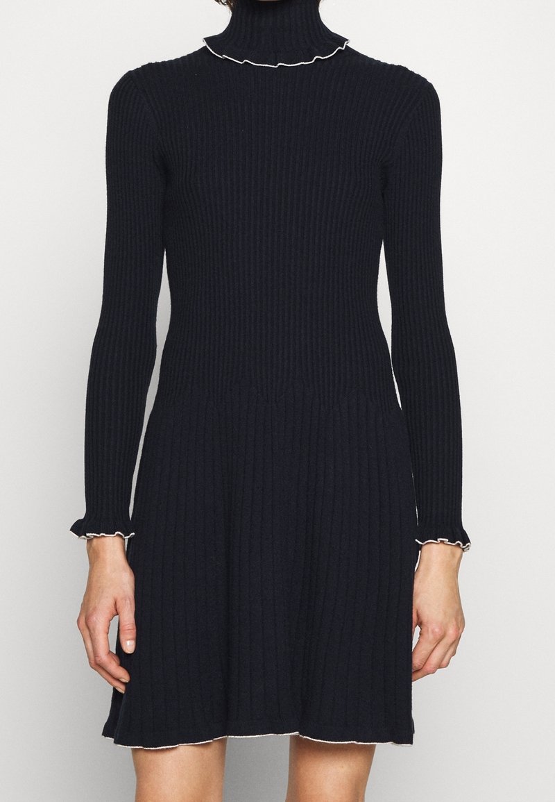 Ribbad mörkblå klänning med hög hals och långa ärmar. Utrustad med vit volangkant vid halsen och ärmsluten. Utsvängd fåll.