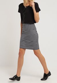 Černý top s krátkým rukávem v kombinaci s úzkou sukní s černobílými pruhy. Model má na sobě lesklé černé boty. Jednoduchý, elegantní design.