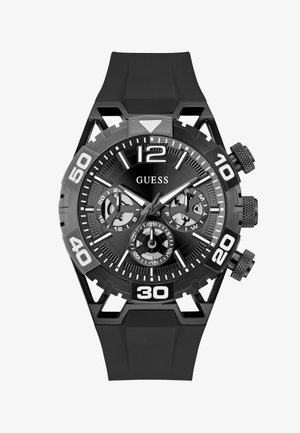 Black Guess wristwatch with large white numerals, three subdials for 24-hour, day, and date, and a black rubber strap.