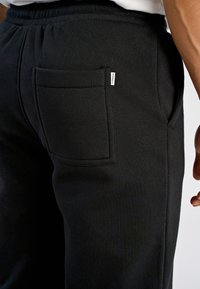 Zwarte joggingbroek met een zichtbare achterzak voorzien van een label. Gemaakt van zachte stof, met een elastische tailleband en een ontspannen pasvorm.