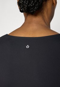 Čierny odev so širokým výstrihom, hladkou textúrou a malým bielym logom pri zadnom krku. Tkanina sa javí ako ľahká a priliehavá.