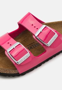 Sandal in vernice rosa con due cinturini regolabili, accessori in argento, soletta in sughero e suola in gomma nera testurizzata.