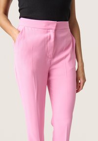 Pantaloni su misura rosa chiaro con tasche laterali e una texture liscia. Presentano una vita aderente e un design a gamba dritta.