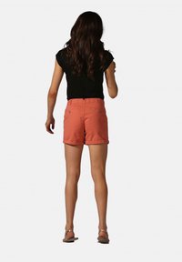 Shorts corail en tissu léger, avec une taille ajustée, un ourlet roulé et deux poches arrière. Portés avec un haut noir à manches courtes.