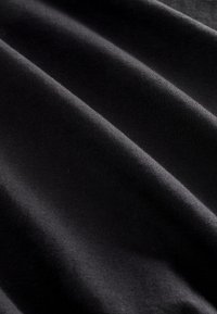 Gros plan d’un tissu noir lisse avec des plis doux et une texture fine visible.