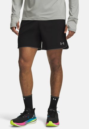 Zwarte sportshorts met een grijze bies en een logo op de zoom. Draagt kleurrijke hardloopschoenen en zwarte sokken met een logo.