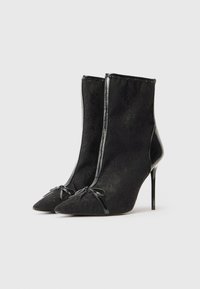 Svarta ankelstövlar med spetsig tå, textilstruktur, glänsande detaljer och dragkedja. Har dekorativa rosetter framtill.