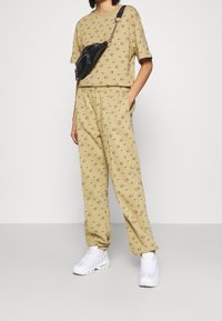 Beige souprava skládající se z trička s krátkým rukávem a volných kalhot, se zaobleným vzorem. Doplněno bílými teniskami a černou crossbody taškou.