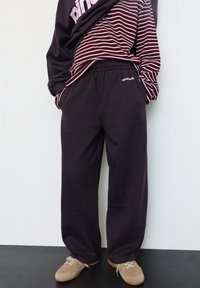 Locker sitzende dunkelgraue Jogginghose aus weichem Stoff, mit elastischem Bund und Seitentaschen, kombiniert mit einem bordeauxroten und weißen gestreiften Shirt.