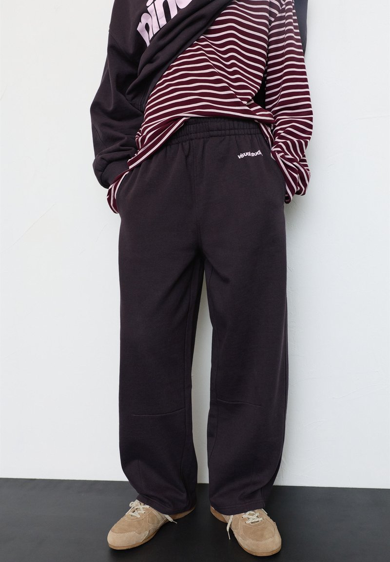 Locker sitzende dunkelgraue Jogginghose aus weichem Stoff, mit elastischem Bund und Seitentaschen, kombiniert mit einem bordeauxroten und weißen gestreiften Shirt.