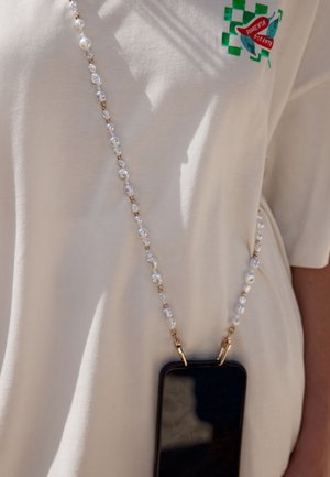 Perlenbesetzter Telefonriemen, quer über dem Körper getragen, auf einem weißen Hemd mit einer grünen und roten Chilischoten-Grafik auf der Brust.