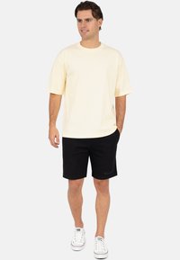 Crème katoenen T-shirt met korte mouwen gecombineerd met zwarte korte broek. Sneakers zijn wit met rode accenten. Casual pasvorm en basic ontwerp.