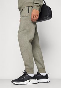 Svijetlosive trenirke s uskim krojem, zatvorenim džepovima i suptilnim detaljima šivanja, uparene s crnim sportskim cipelicama.